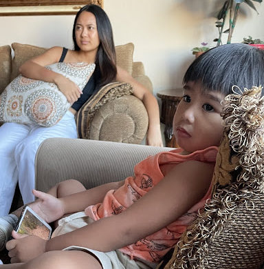 Yasmin Samoy and a sibling sit on a couch, watching television.
