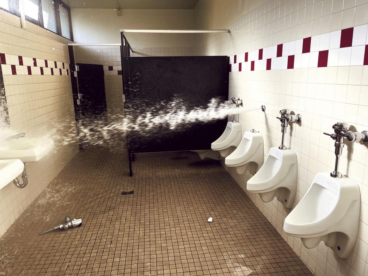 A vandalised men's bathroom, water spraying from one of the urinals.