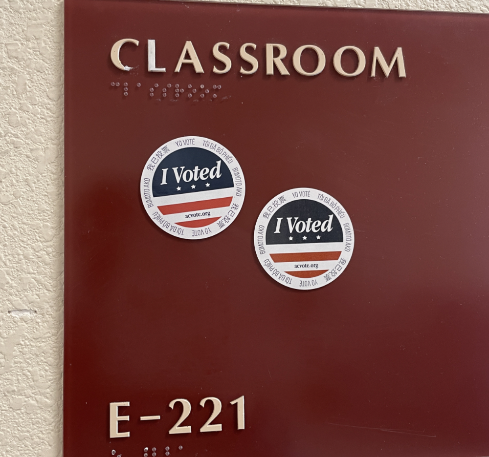 Brown sign that says 'CLASSROOM' on the top, 'E-221' at the bottom left, and has two 'I Voted' stickers.