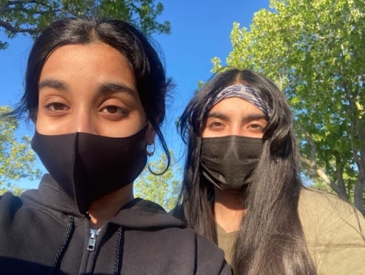 Hanya Hussain (on the right), in a brown shirt, wearing a bandana and her friend in a black sweater (on the left), both wearing black masks, against the backdrop of trees and the blue sky.