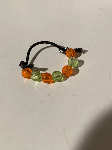 A ring with green and orange alternating beads on a black thread.