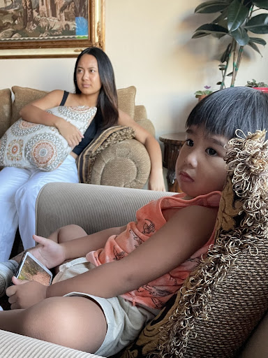 Yasmin Samoy and a sibling sit on a couch, watching television.